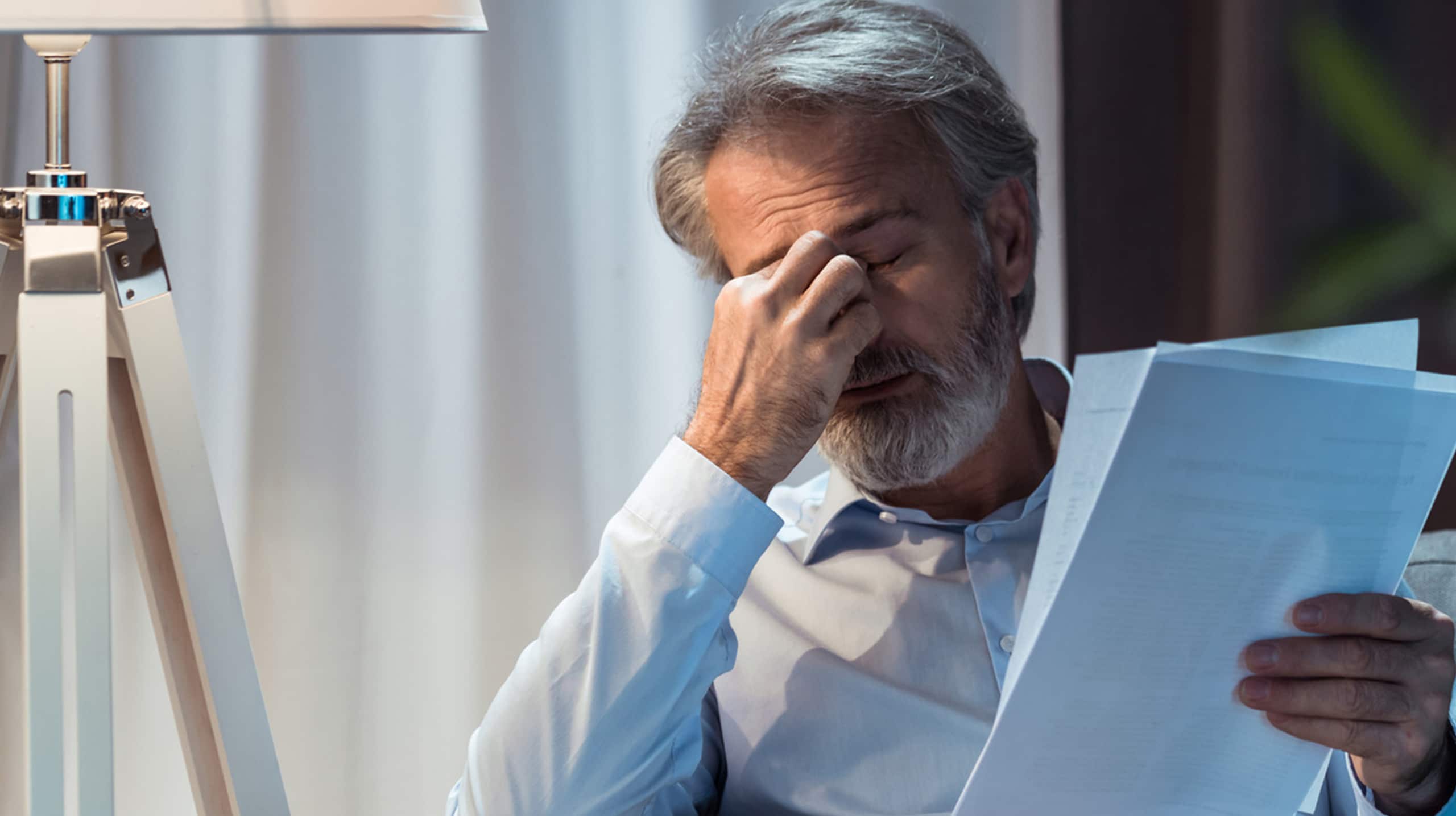 Homme senior fatigué se pinçant l’arête du nez en lisant des documents